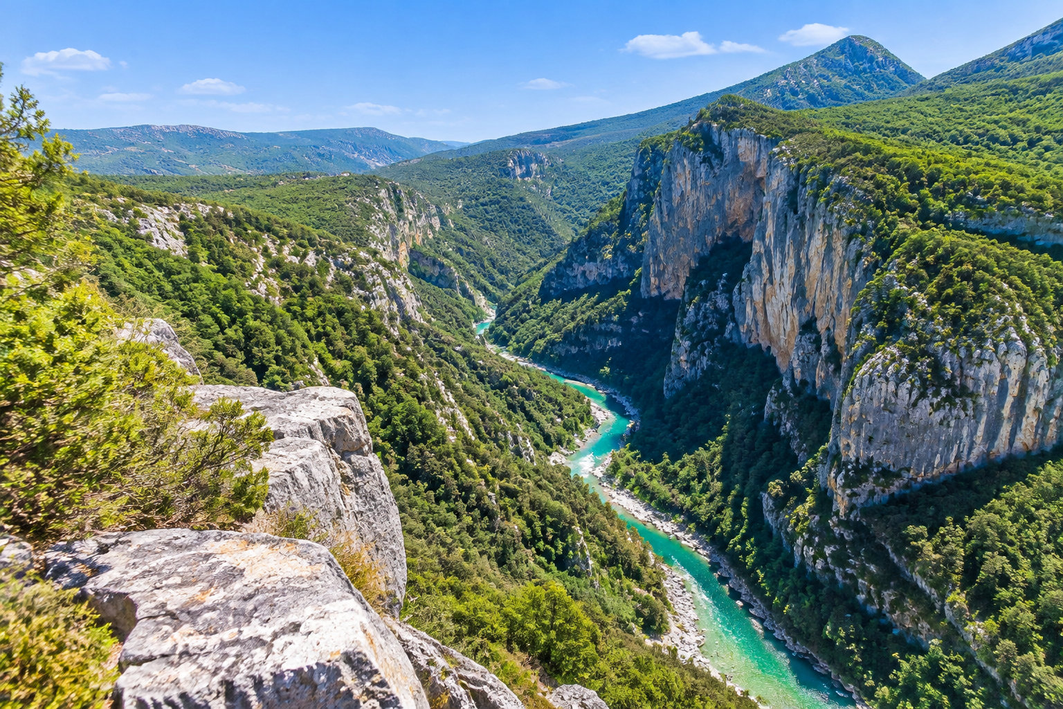 Une rivière turquoise serpente au fond d’un profond canyon bordé de falaises rocheuses et de versants boisés.