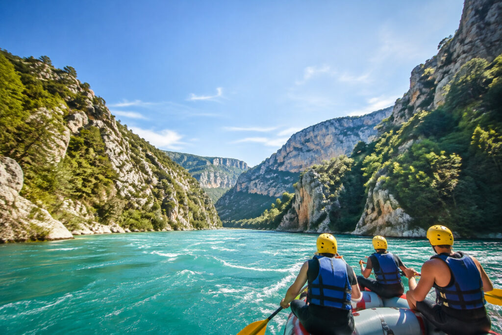 Trois personnes en gilet de sauvetage et casque jaune rament dans un raft sur l'eau turquoise des Gorges du Verdon.